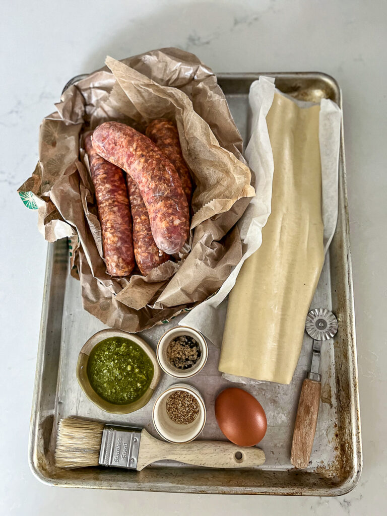 sausage roll ingredients on a tray. sausage, puff pastry, pesto, egg