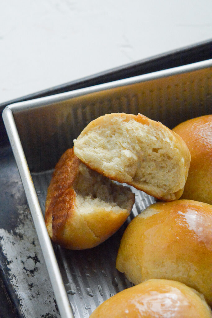 vertical close up of dinner rolls in pan with one cut in half